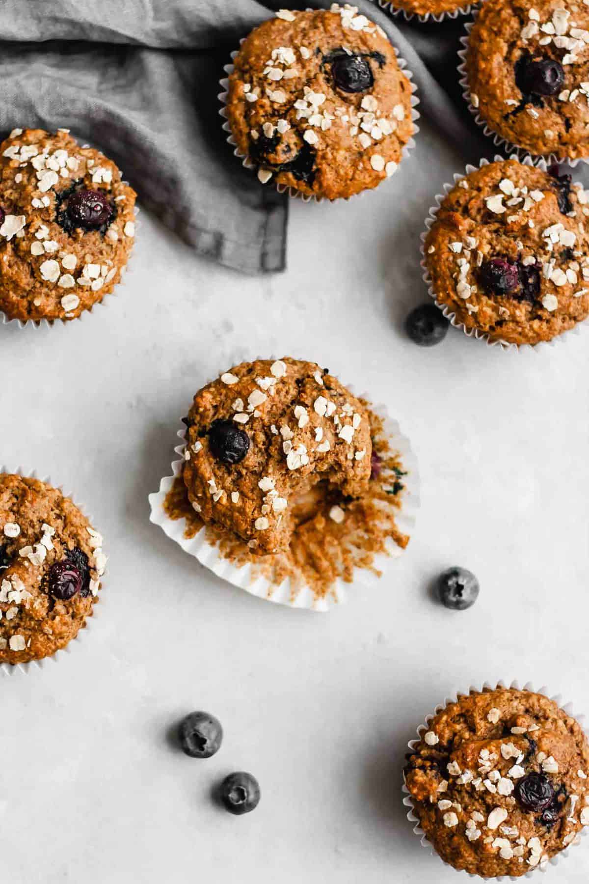 A group of blueberry muffins on a table, one with a bite taken out of it.