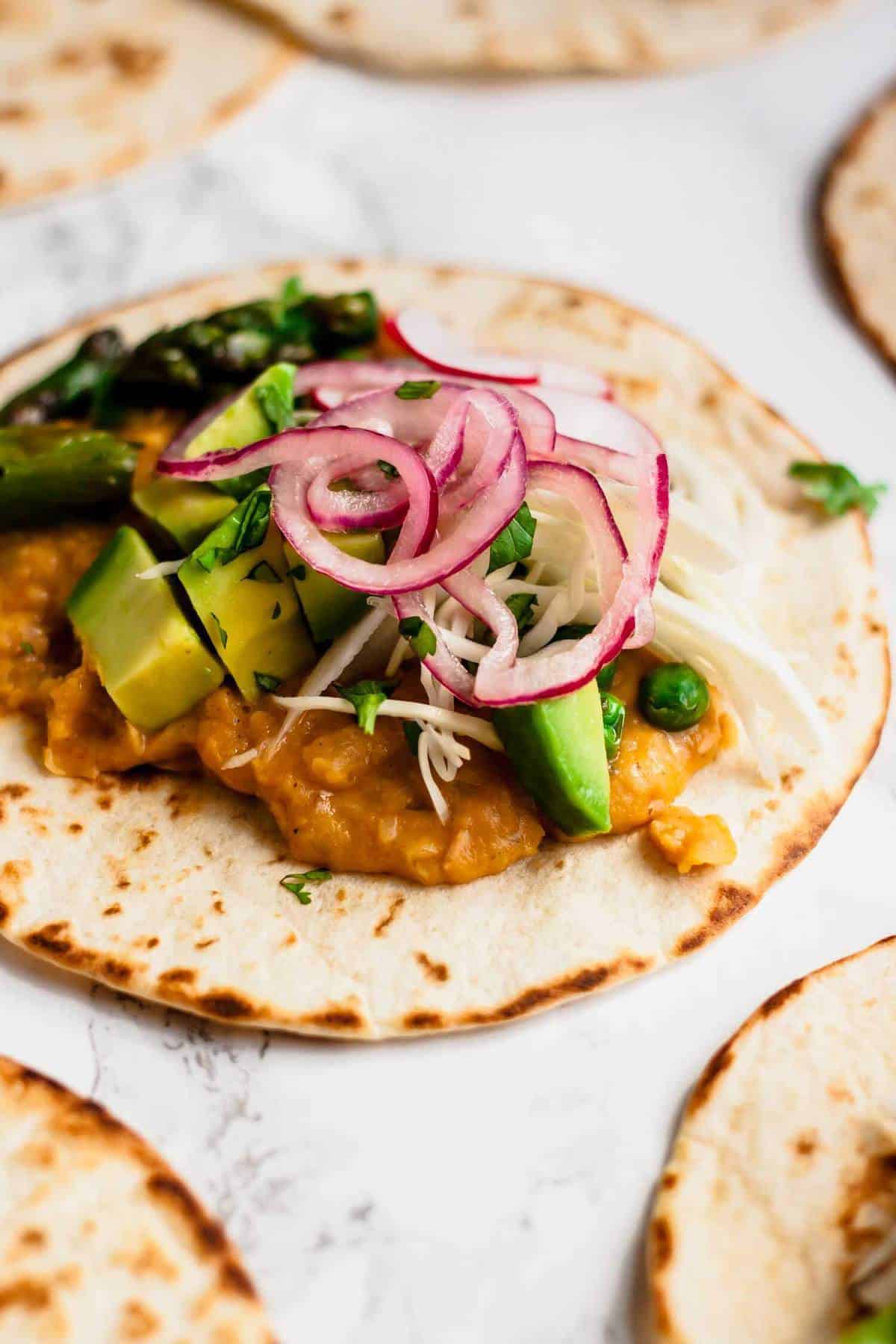 Close up showing refried beans and toppings on a corn tortilla. 