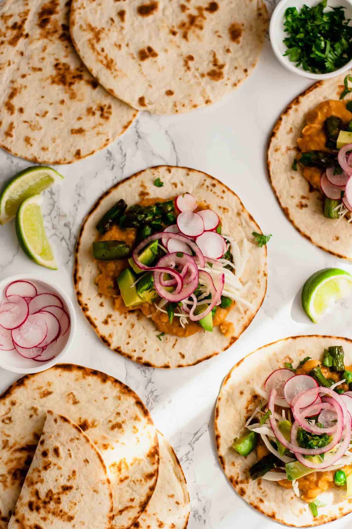 Multiple vegan tacos with limes and pickled onions nearby.