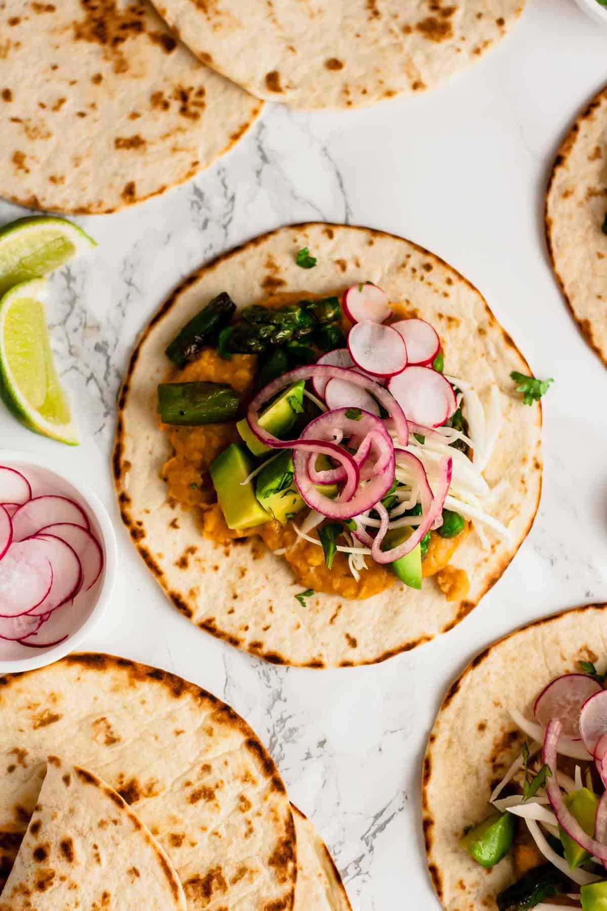 A vegan taco with avocado, pickled onion and radishes on top.