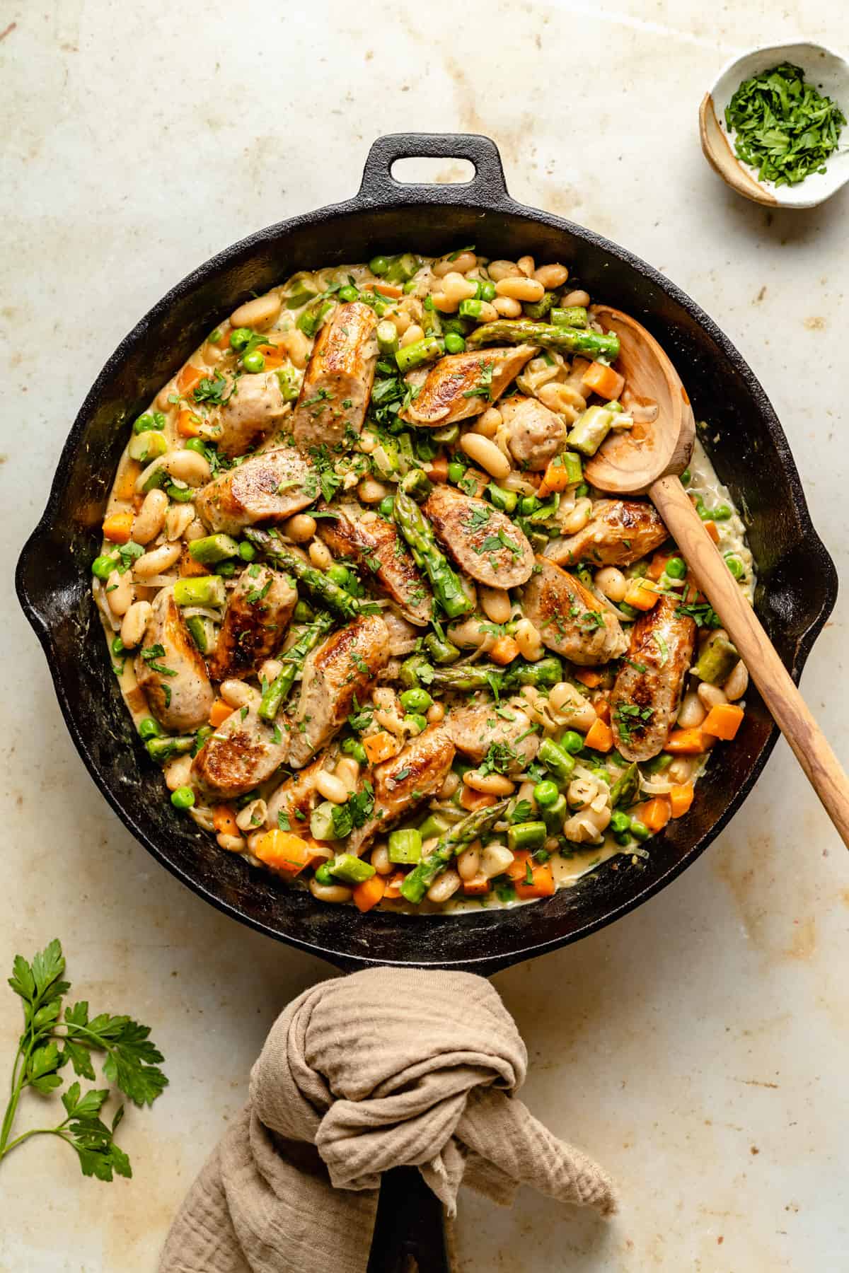 Creamy Chicken Sausage Skillet finished with a napkin around the handle and a wooden spoon to serve.