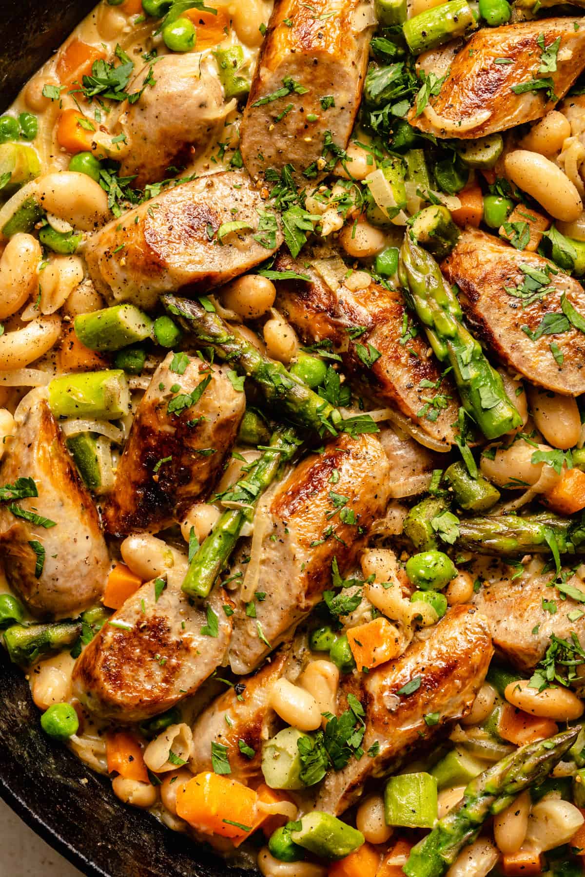 shot of finished dish of creamy chicken sausages and vegetables in a cast iron skillet with spoon.