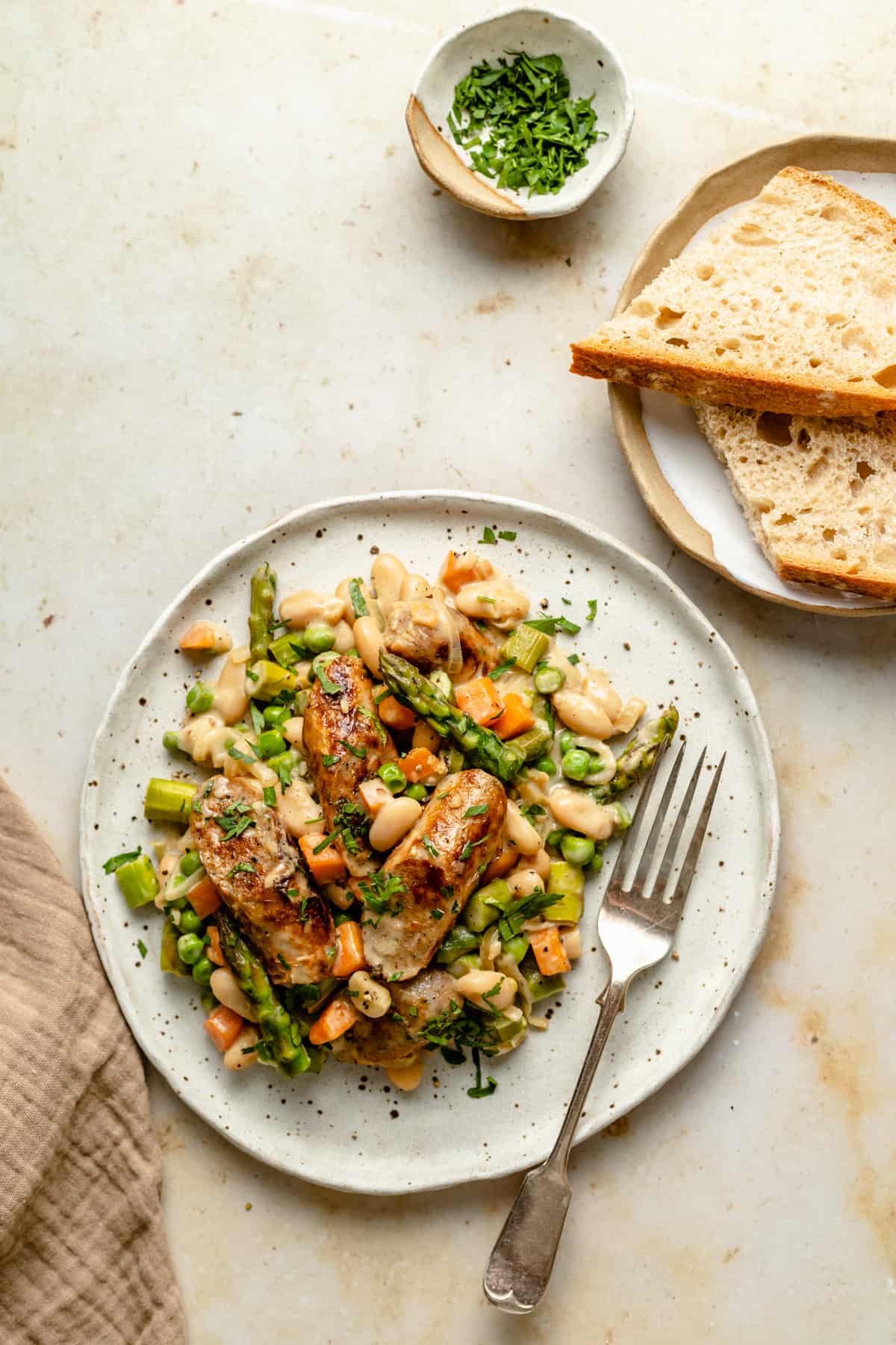 A serving of chicken sausage skillet and vegetables served on a small plate with a fork and a side of bread.