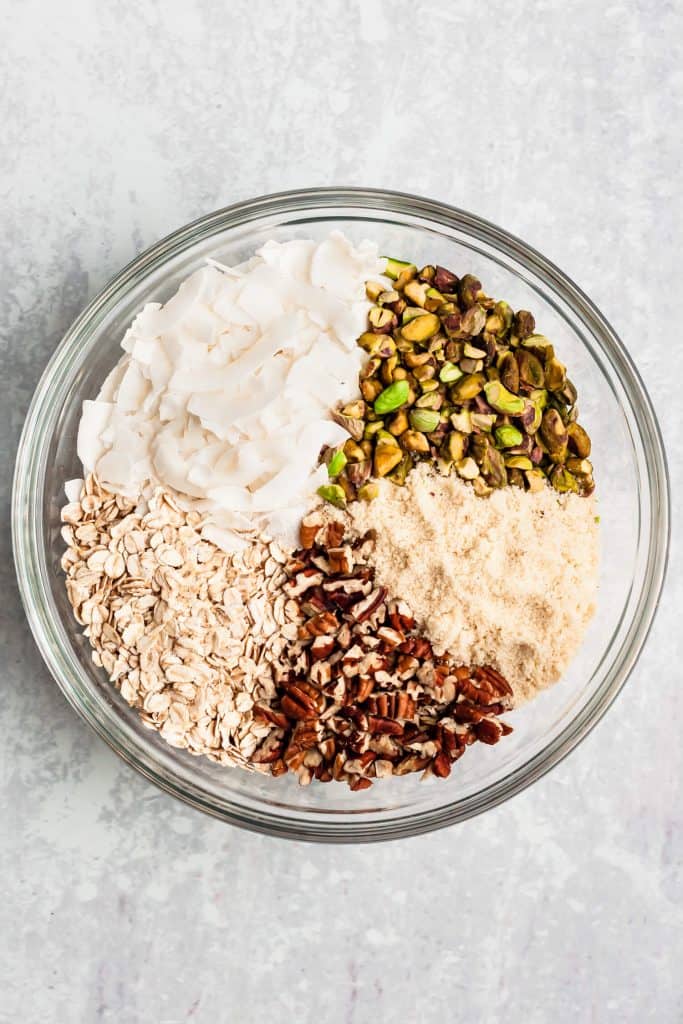 A bowl showing the ingredients of granola including, oats, coconut and nuts.