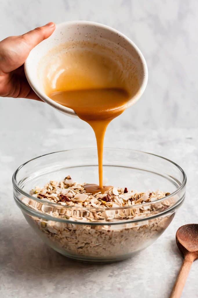 shot of wet ingredients being poured from a bowl into a bowl of dry granola ingredients