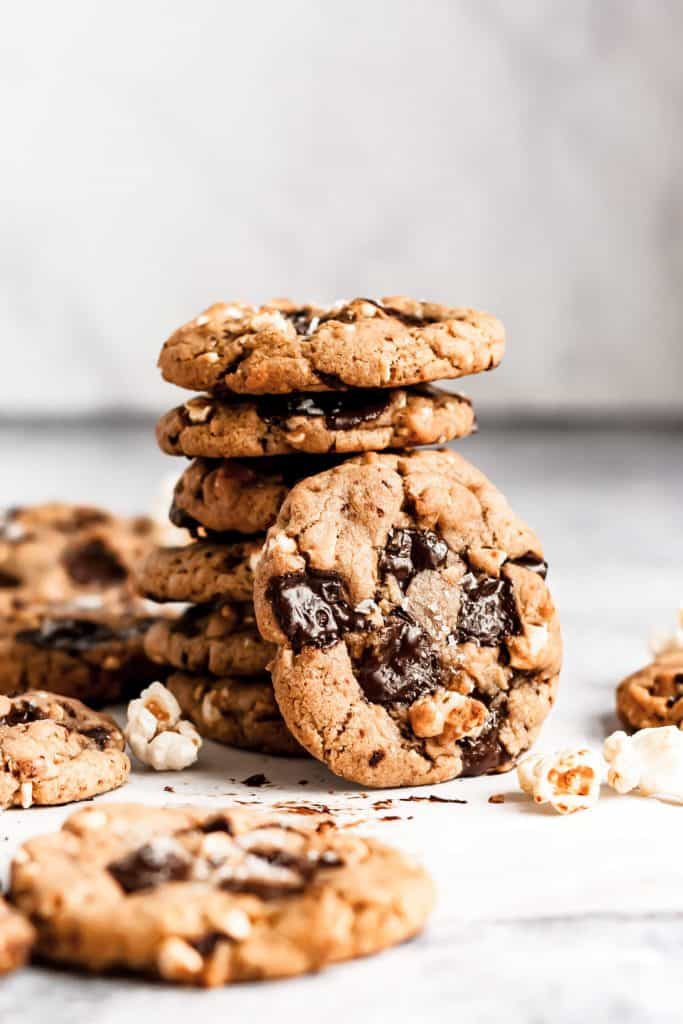 a stack of popcorn chocolate chip cookies with one cookie leaning against the stack and popcorn scattered around