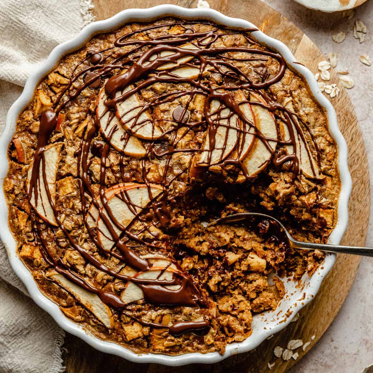 A baked oatmeal half served up from a dish on a wooden board with a spoon and napkin. 