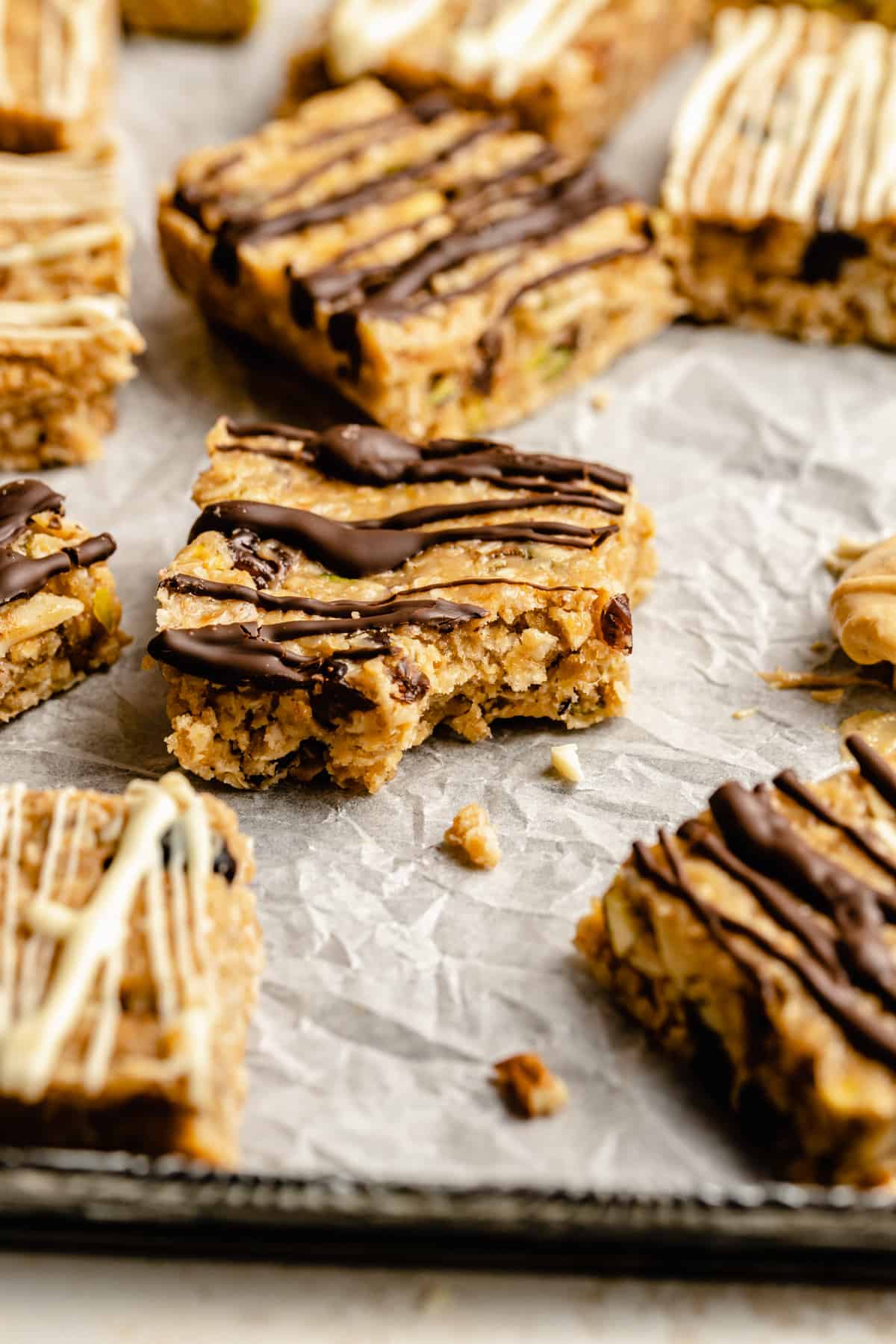 no bake granola bars drizzled with chocolate on a piece of crumpled parchment paper with a bite taken out.