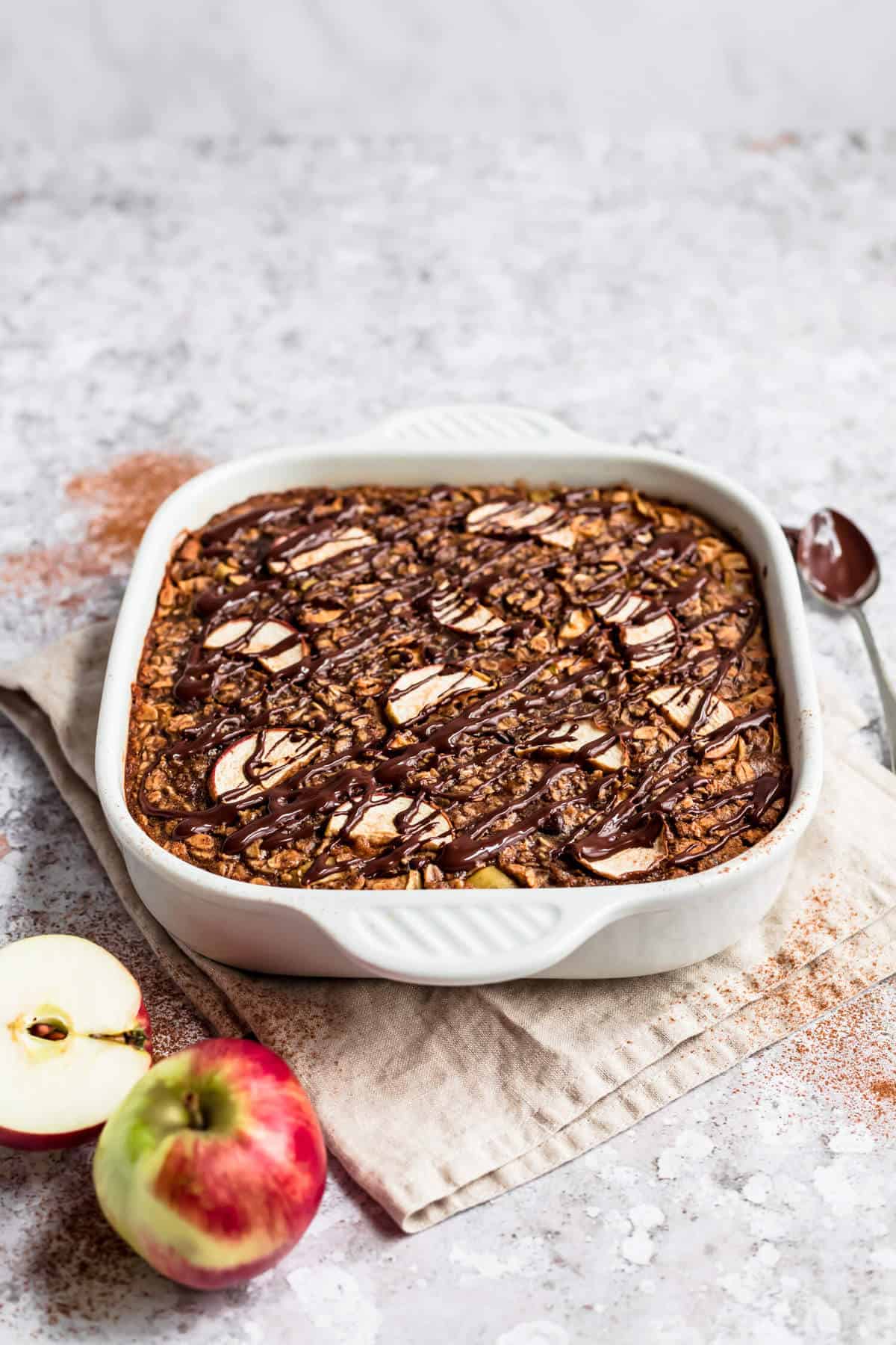 apple baked oatmeal in a ceramic dish on a napkin, drizzled with dark chocolate