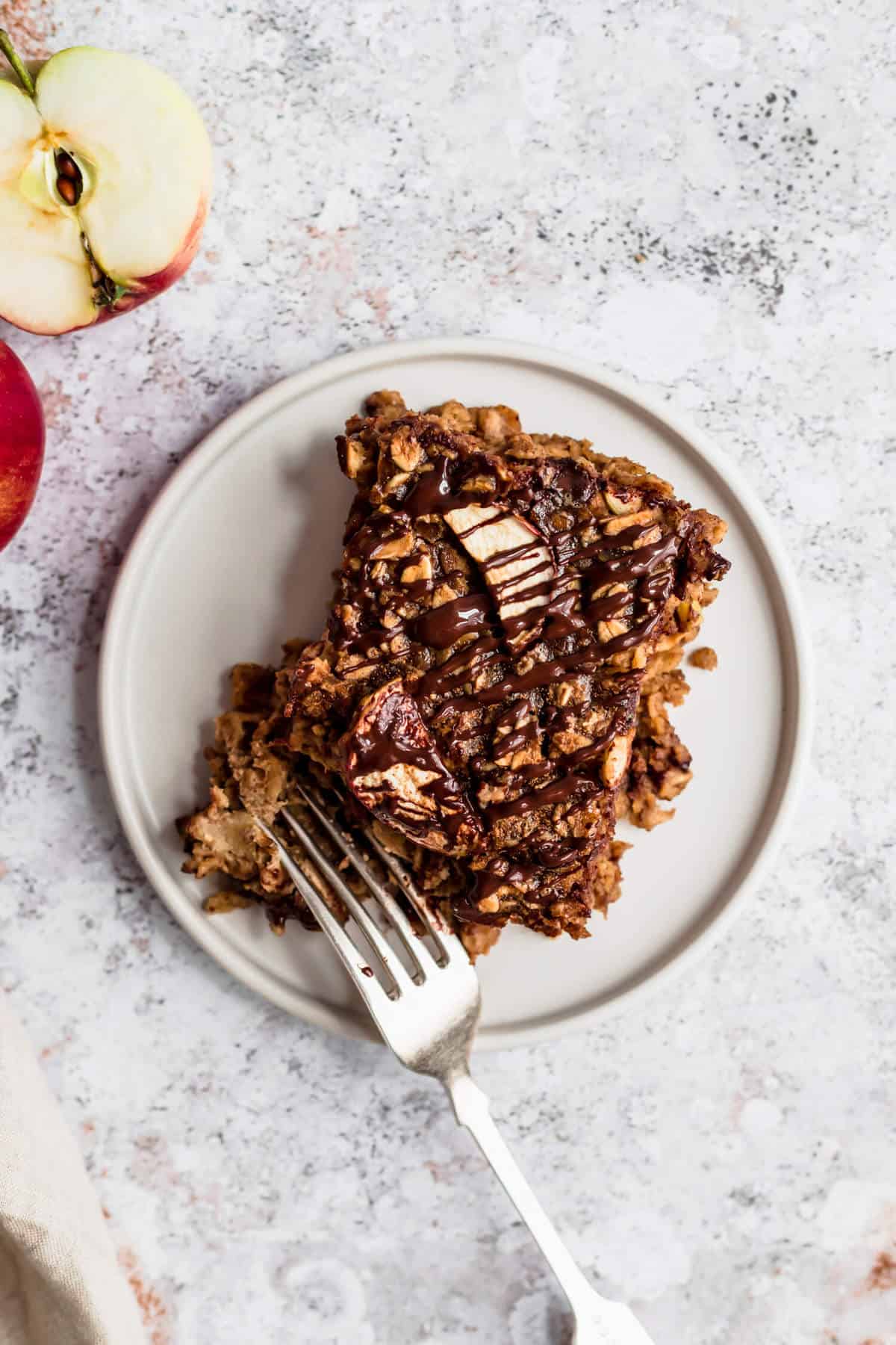 a slice of baked oatmeal on a plate with a fork and half an apple to the side