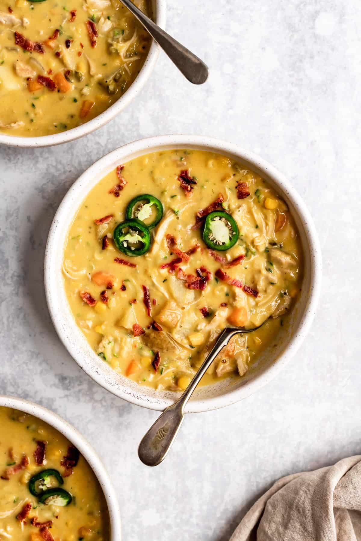 bowl of corn chowder with a spoon in it, topped with bacon and jalapeno slices