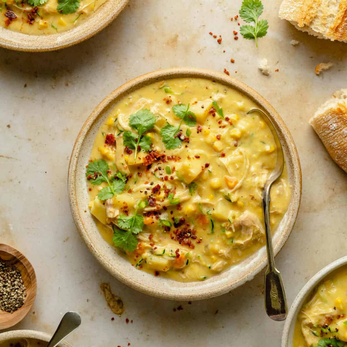 Chicken corn chowder in a bowl with a spoon with coriander and bacon crumbs on top and bread