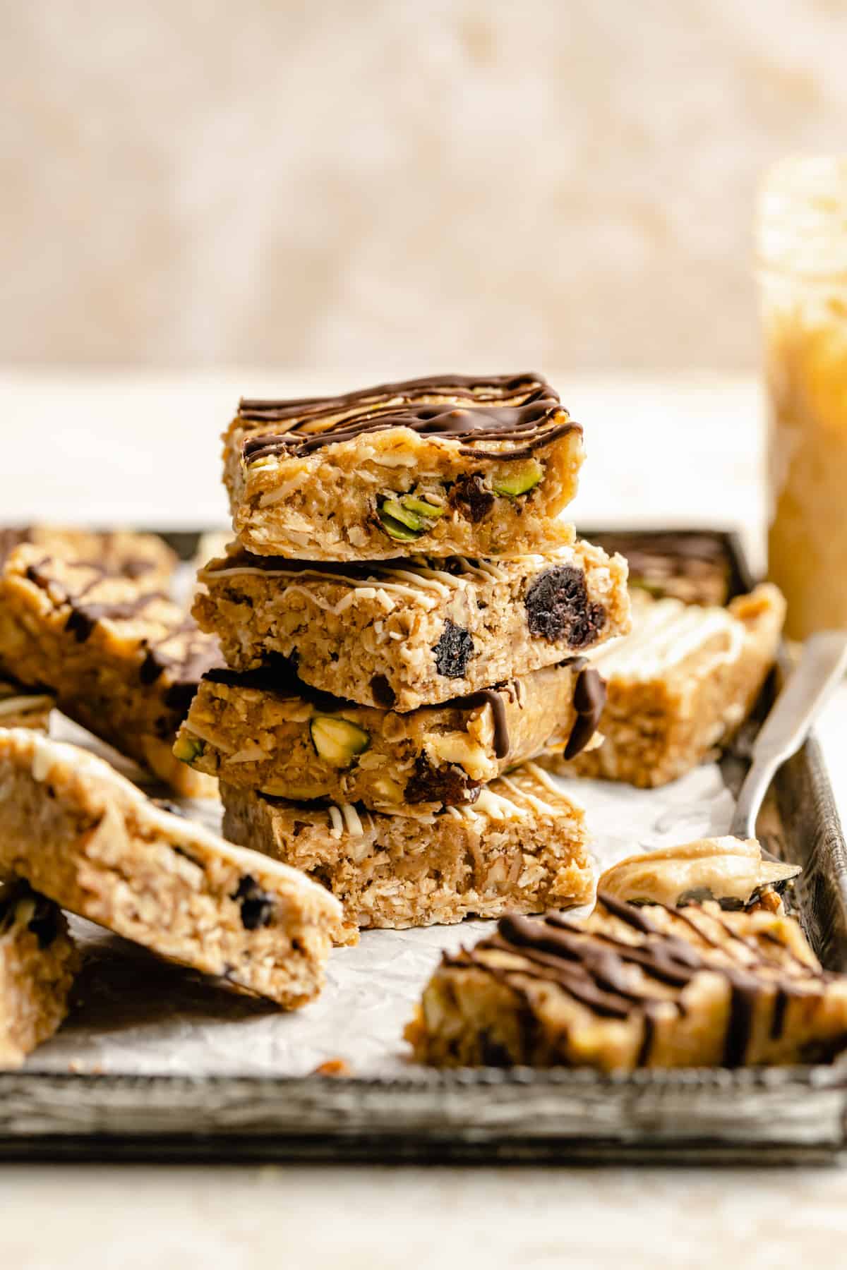 A stack of no bake granola bars with chocolate drizzled over the top and a spoon of cashew butter nearby.
