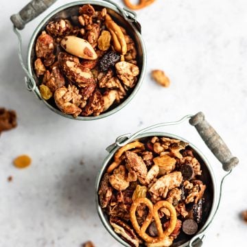 Two small metal buckets filled with maple almond butter snack mix and some pieces scattered around