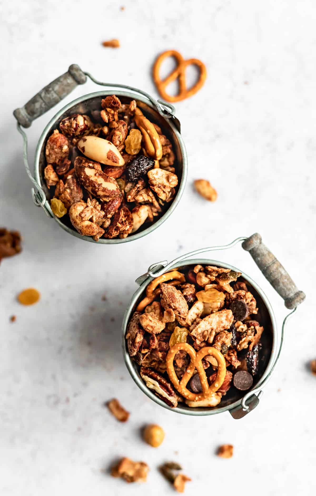 Two small metal buckets filled with maple almond butter snack mix and some pieces scattered around