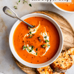 A bowl of soup with cream and herbs on top with spoon