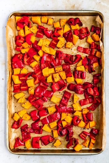Butternut squash and red pepper on a baking sheet with spices before baking.