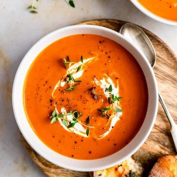 A bowl of butternut squash and red pepper soup with cream and herbs on top.