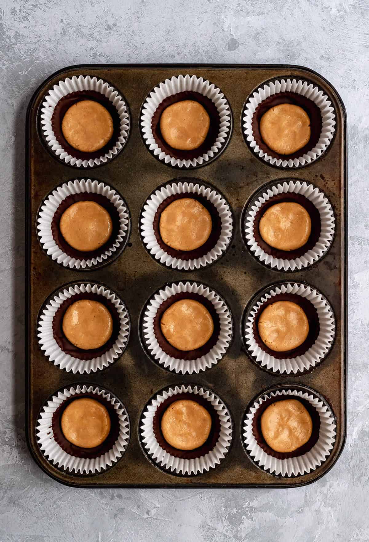 a muffin tin with paper liners filled with chocolate and cashew butter patties