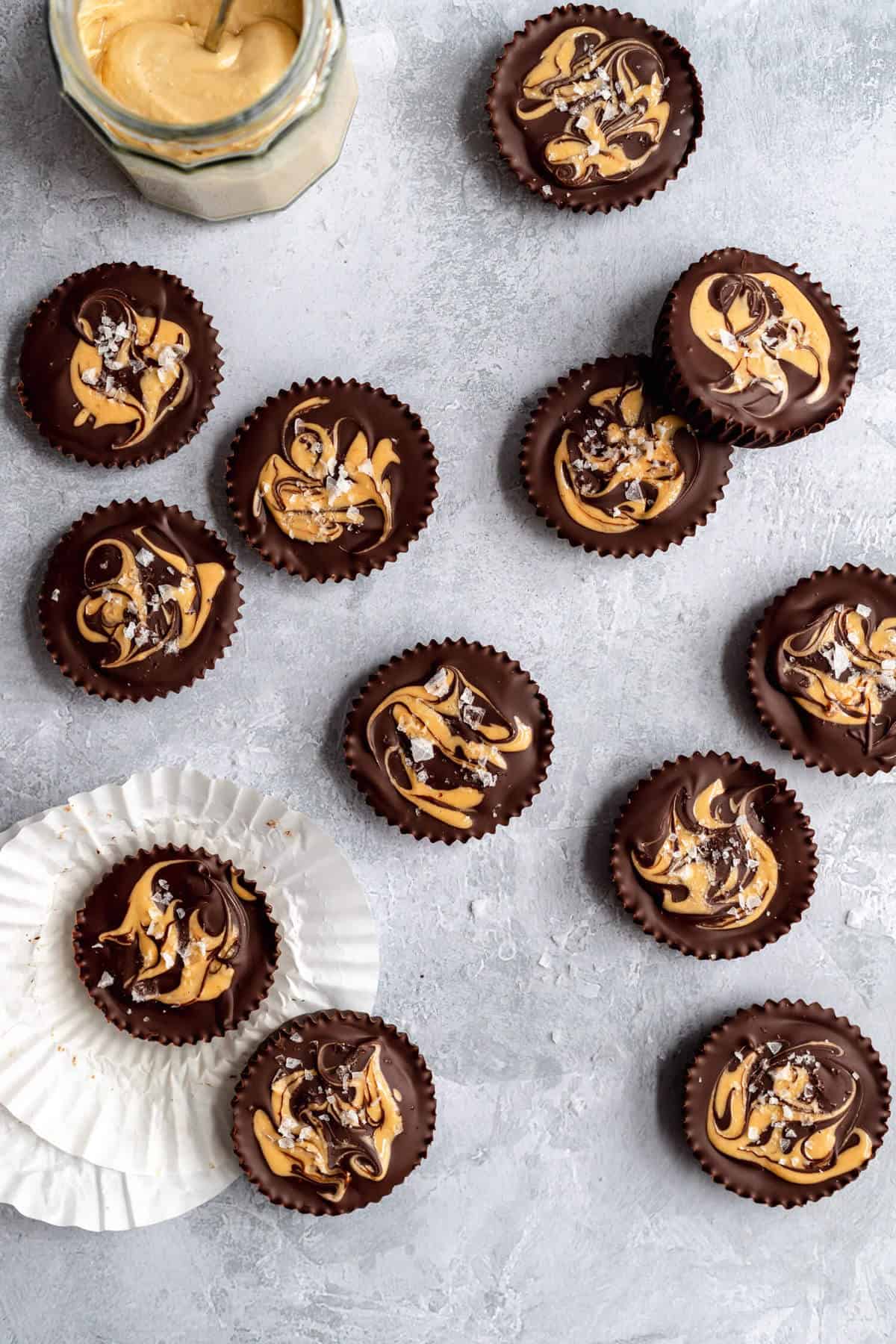 dark chocolate cashew butter cups on a grey surface, with some white paper muffin liners on the side