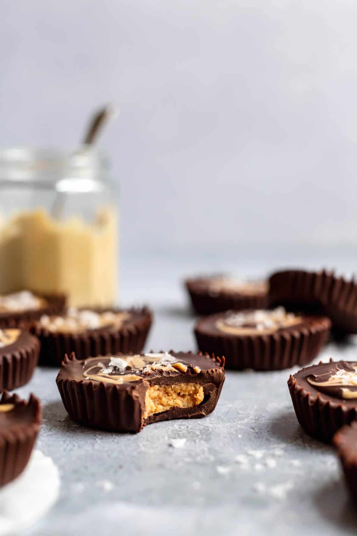 a cashew butter cup with a bite taken out and more cashew butter cups and a jar of cashew butter in the background
