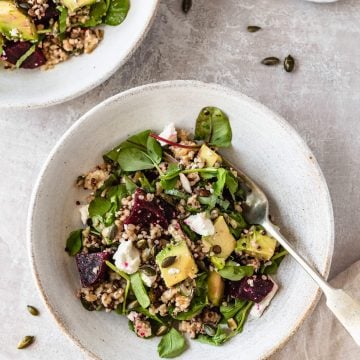 a bowl of salad with a fork on a light background with pumpkin seeds scattered around