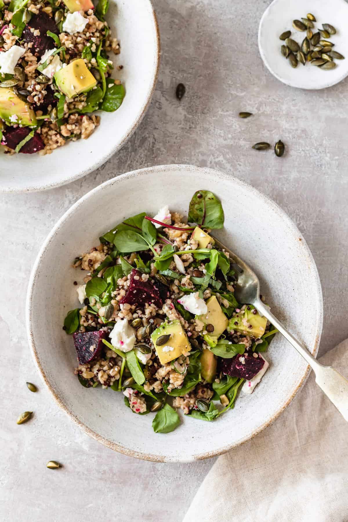 a bowl of salad with a fork on a light background with pumpkin seeds scattered around