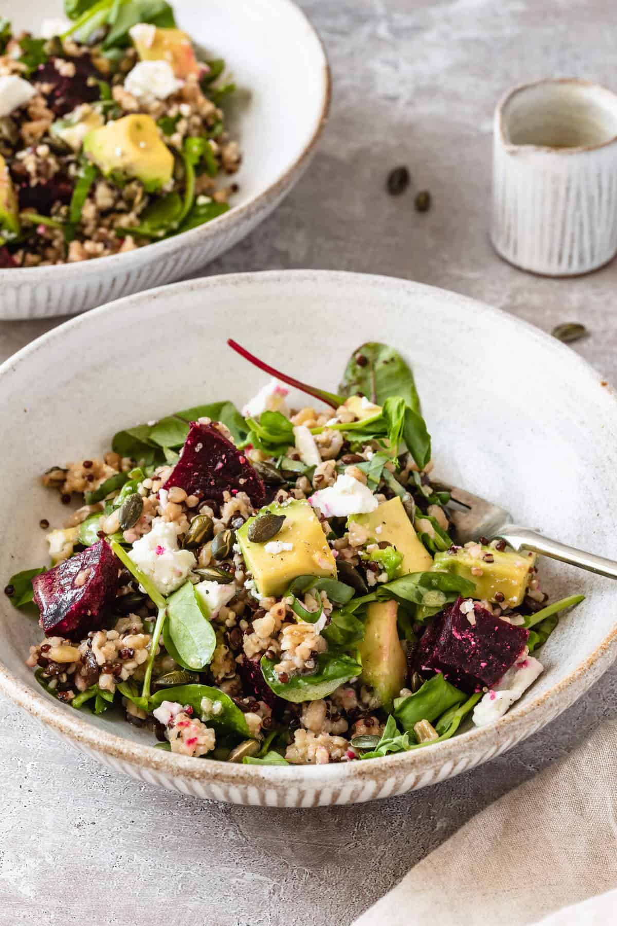 A bowl of beetroot and feta salad on a plate with a fork.