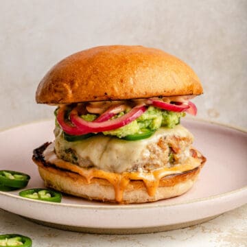 Jalapeño turkey burger on a plate loaded with smashed avocado and pickled red onions.