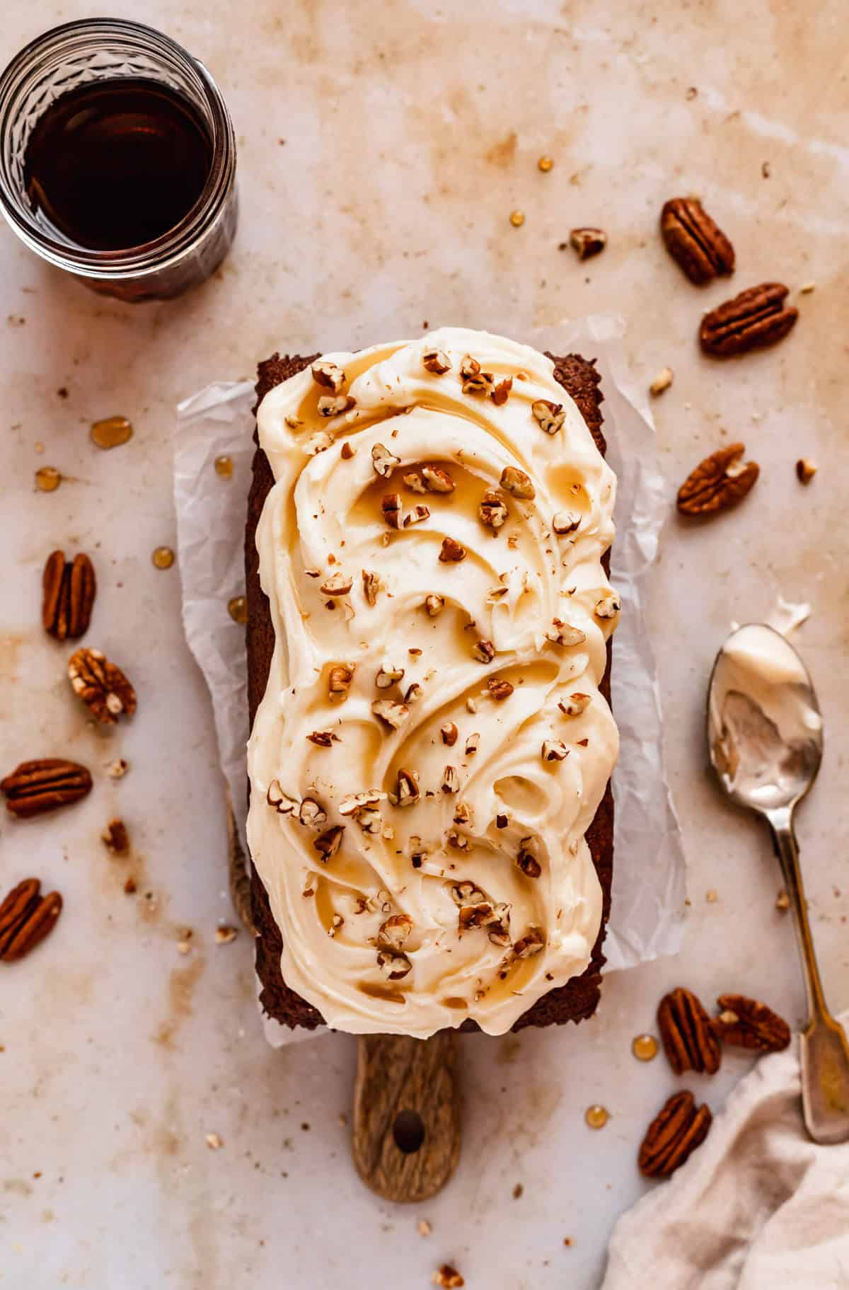 a loaf of banana bread swirled with cream cheese frosting on a wooden board with pecans scattered around
