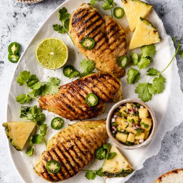 grilled chicken breasts on an oval platter with a bowl of pineapple salsa, jalapeno slices, lime and pineapple slices