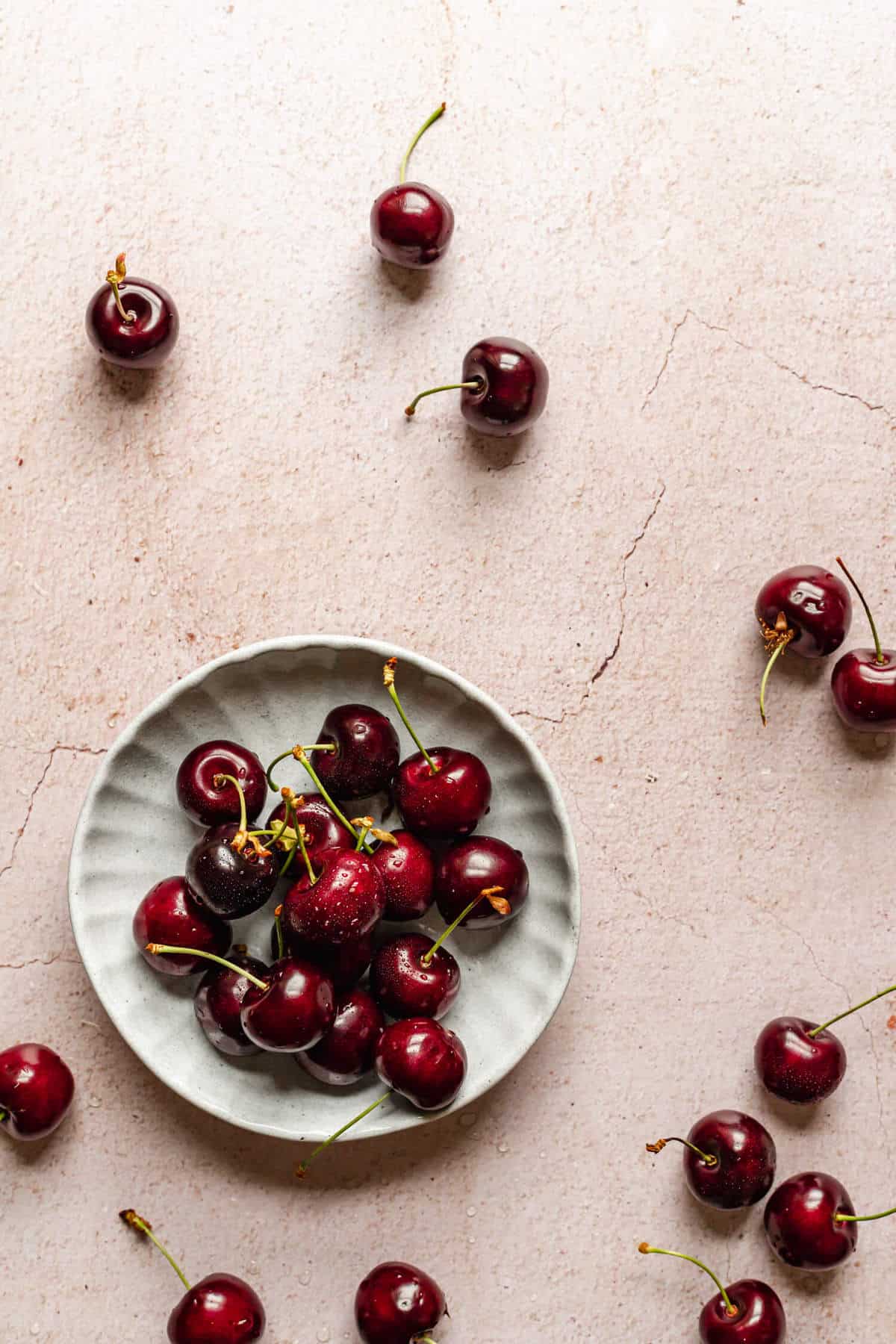 a small dish of cherries with a few more cherries scattered around