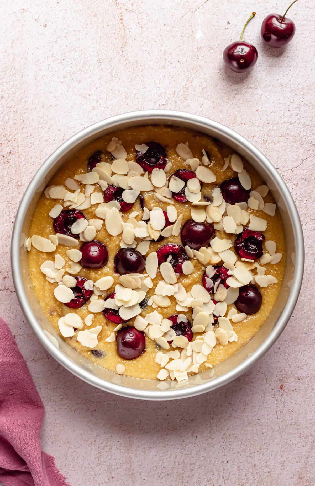 a cake tin filled with unbaked cake batter and topped with halved cherries and flaked almonds