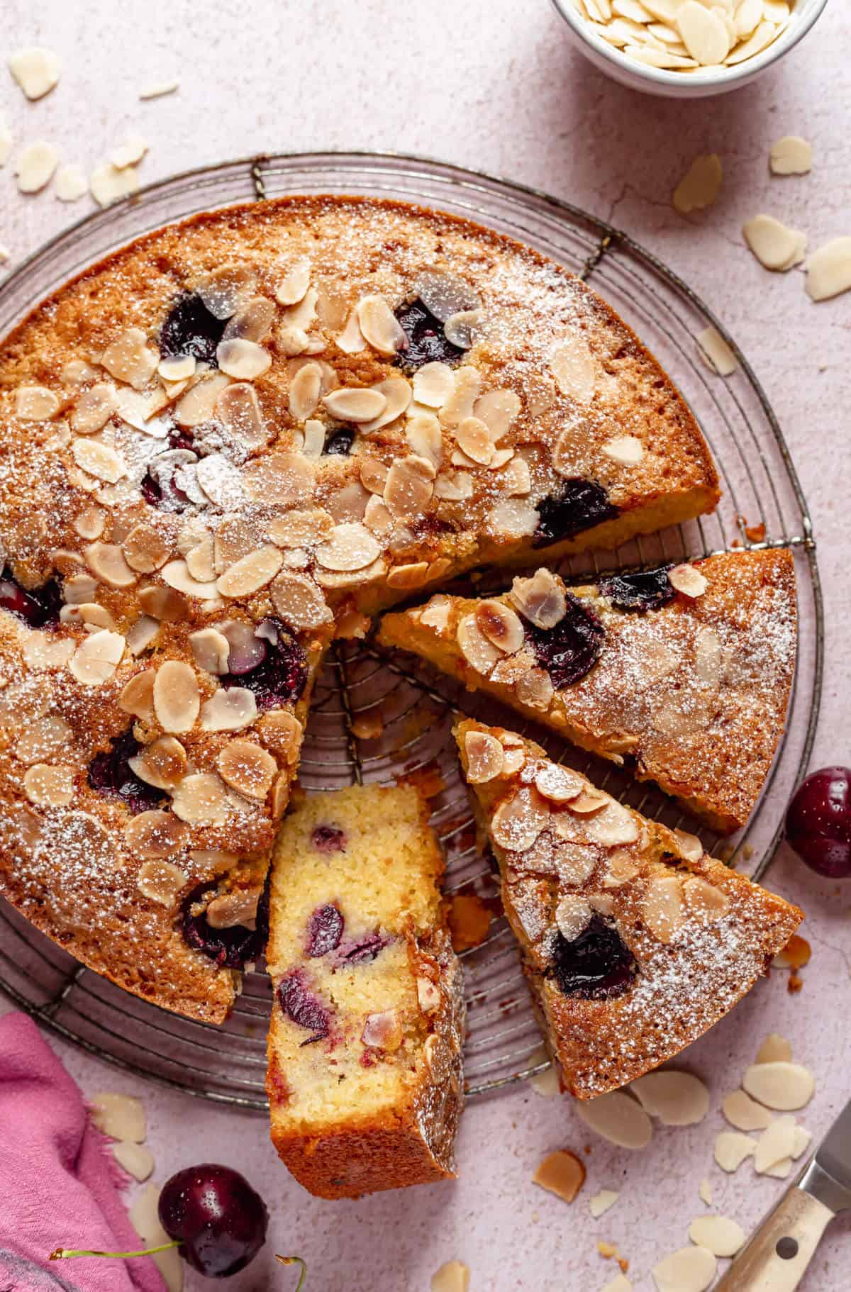 cherry almond cake on a round wire rack with a few slices cut