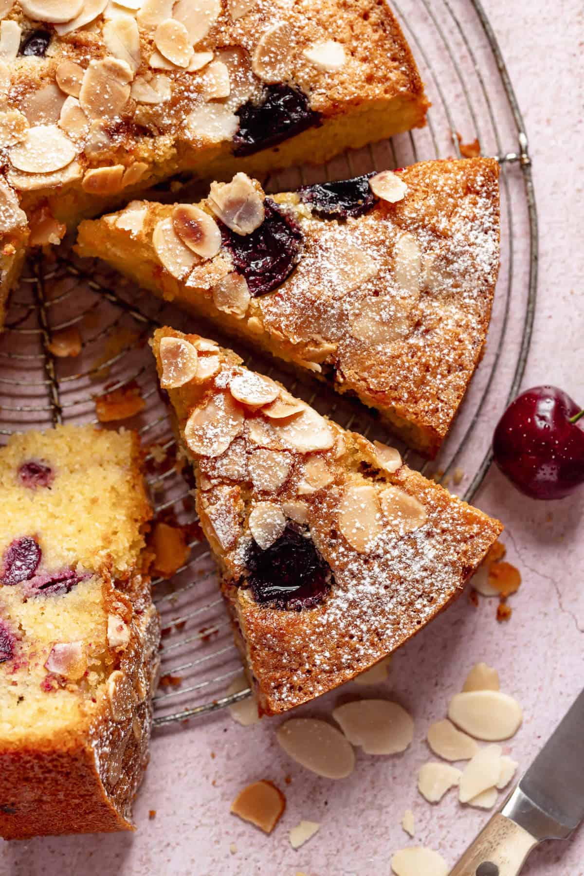 close up of some slices of cake on a wire rack with a cherry and some flaked almonds on the side