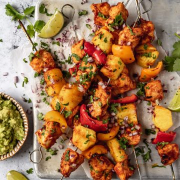 chicken, pineapple and bell peppers on skewers on an upturned baking sheet, sprinkled with herbs