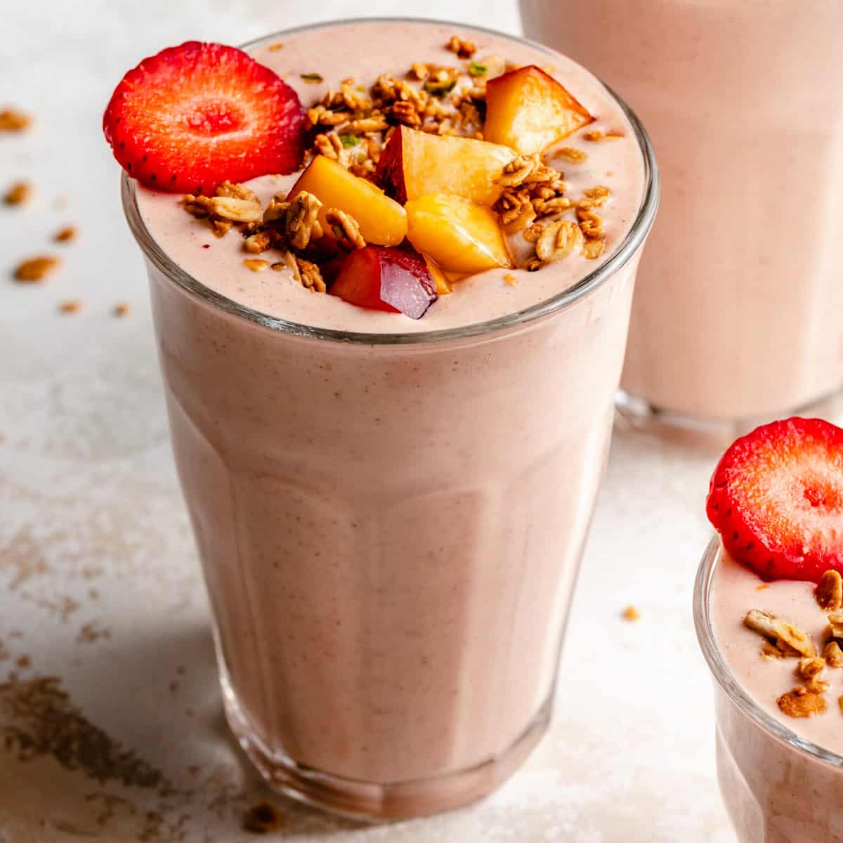 A glass of strawberry peach smoothie with fruit and granola on top. 