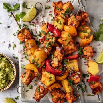 chicken, pineapple and bell peppers on skewers on an upturned baking sheet, sprinkled with herbs