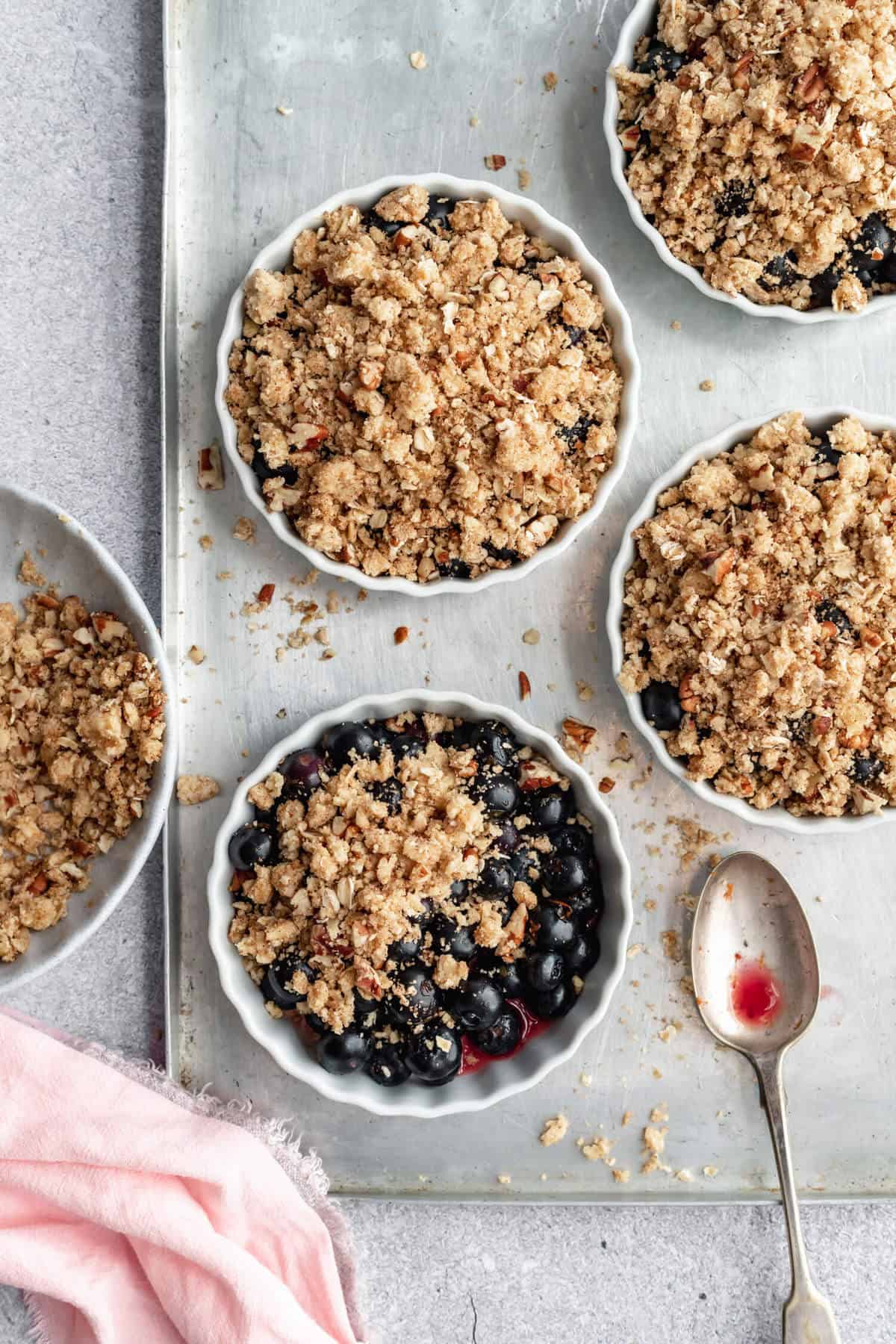 a baking sheet with four unbaked fruit crisps in the process of being assembled, with a spoon on the side