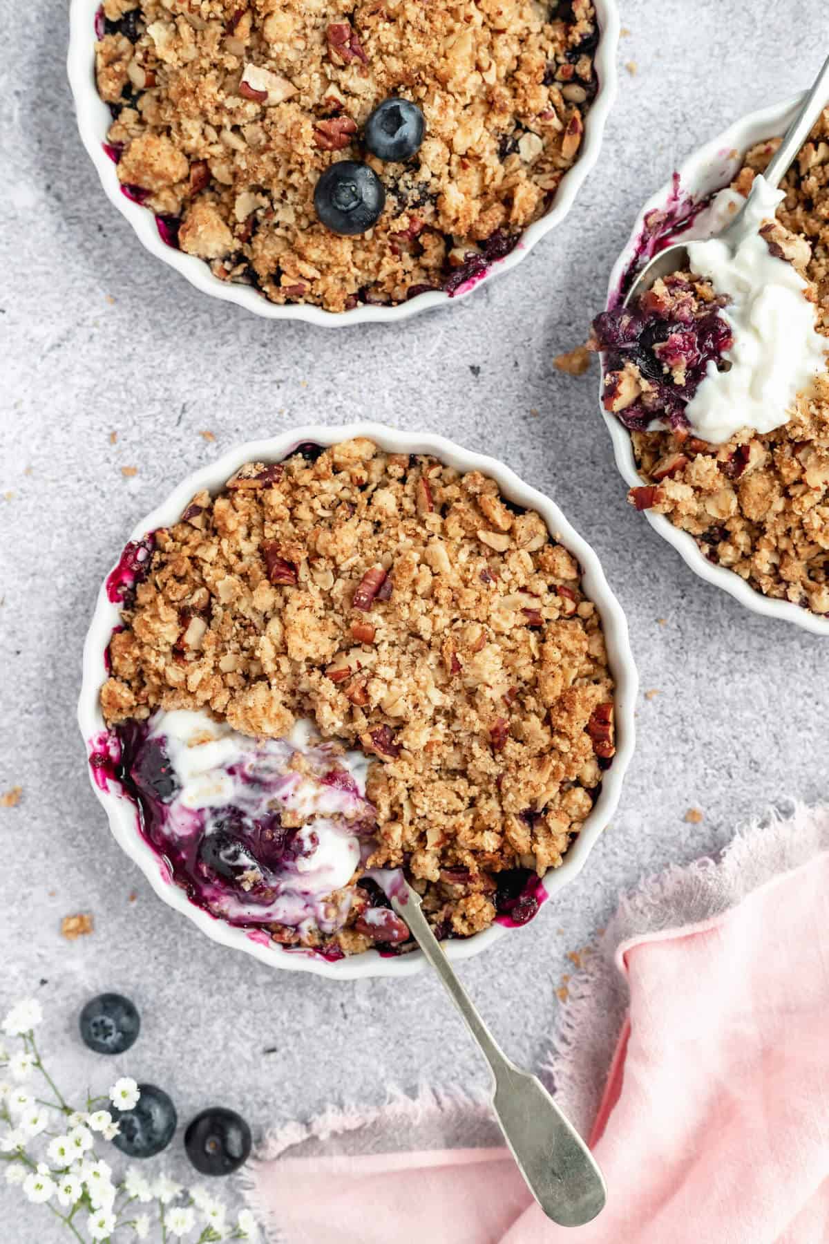 close up of a blueberry pecan crisp topped with greek yoghurt with a spoon