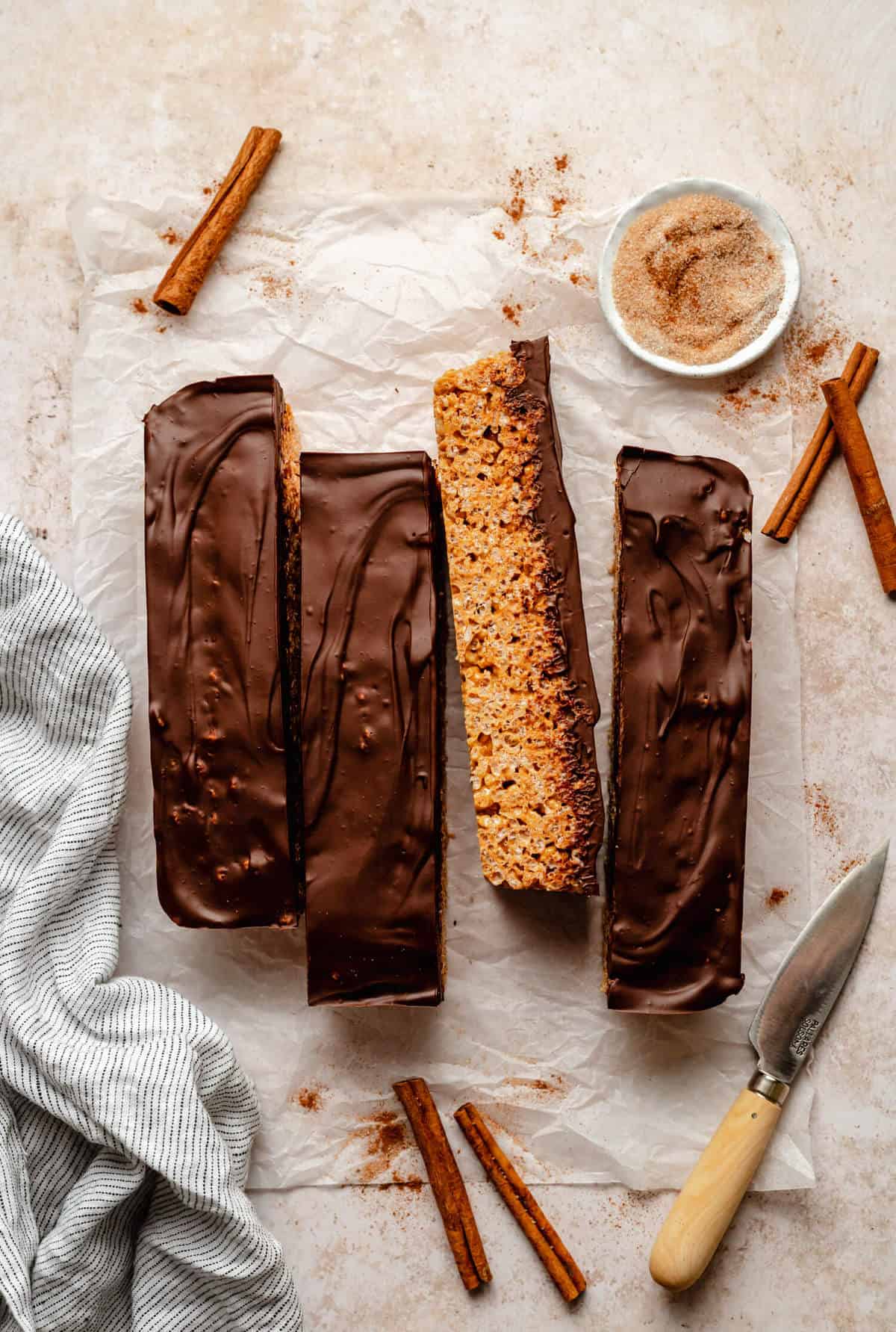 Photo of the set rice krispie bars sliced into four lengths with a knife and cinnamon sticks surrounding