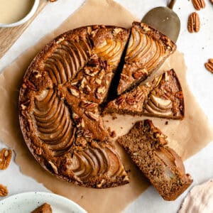 Pear Cake on parchment with three slices cut and one being pulled away.