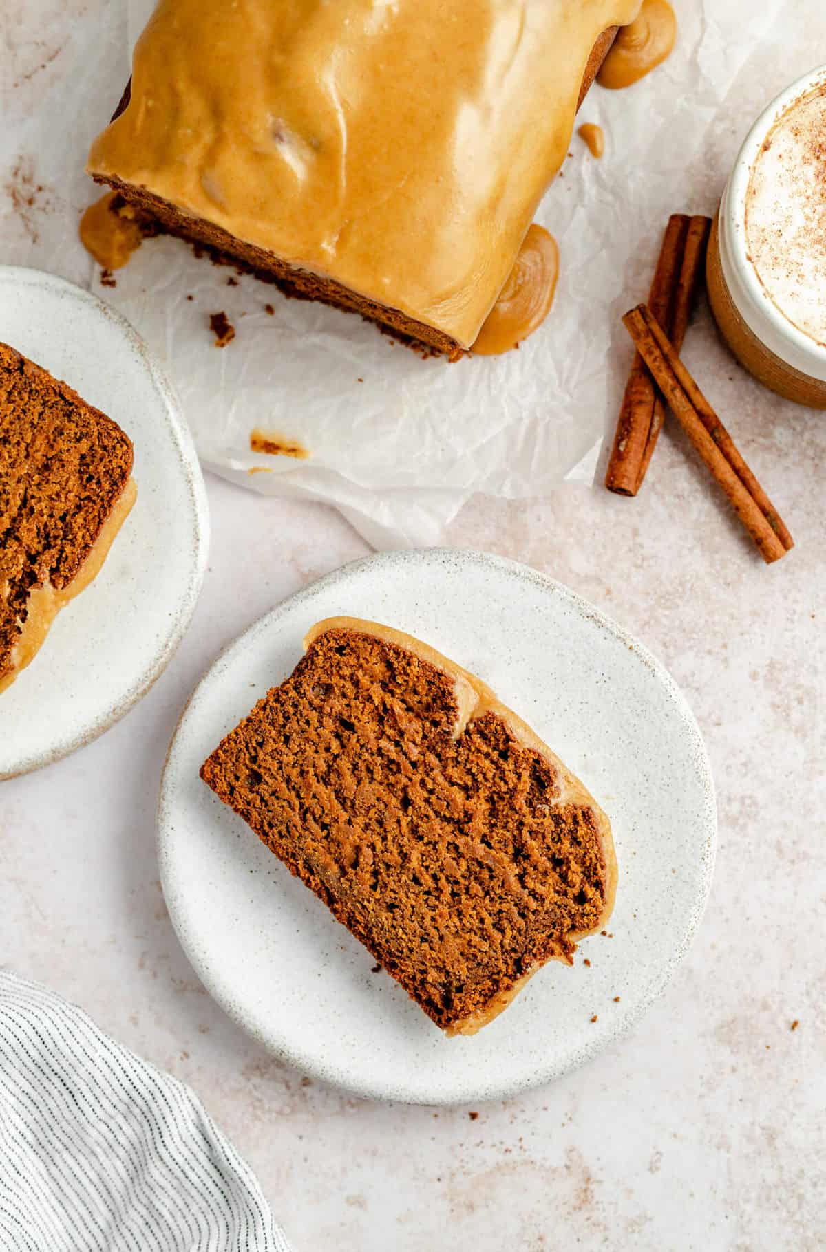 A plate with a slice of pumpkin gingerbread with the cake above and a coffee to the side.