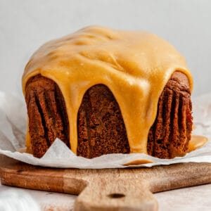 Pumpkin gingerbread side on with brown butter caramel glaze drizzling down the sides on a chopping board with parchment paper.