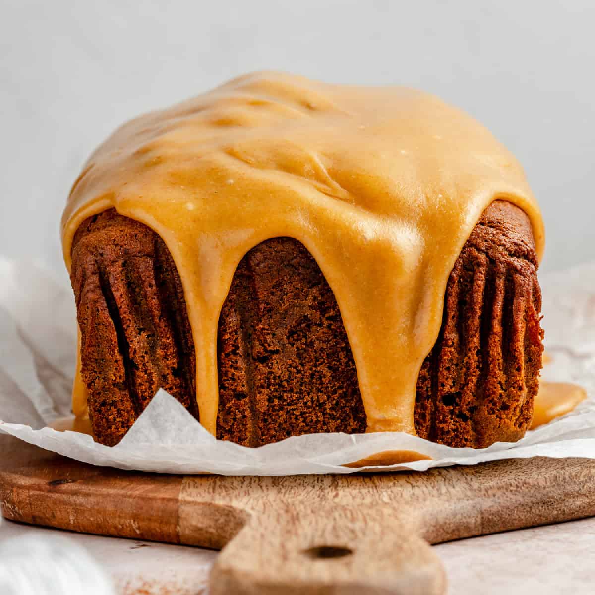 Pumpkin gingerbread on a chopping board with brown butter caramel glaze dripping down the sides. 