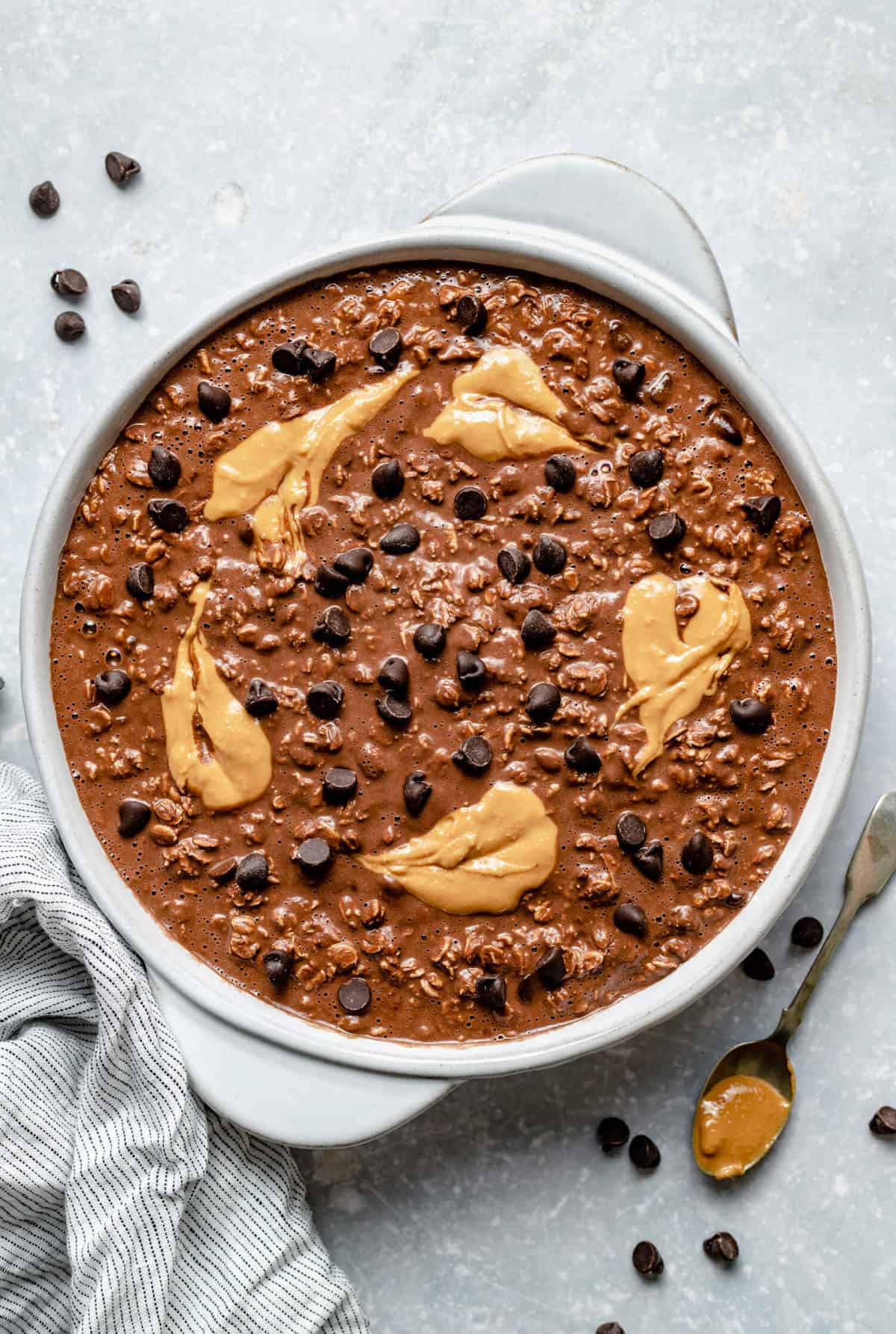a round baking dish filled with the unbaked oatmeal mixture, topped with chocolate chips and peanut butter swirls and with chocolate chips on the side
