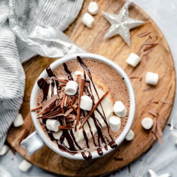 Peppermint hot chocolate with cream, marshmallows and chocolate drizzled on top on a board.