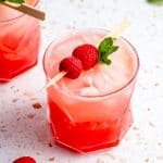 Two glasses of raspberry mocktail with ice and a skewer of raspberries on top.