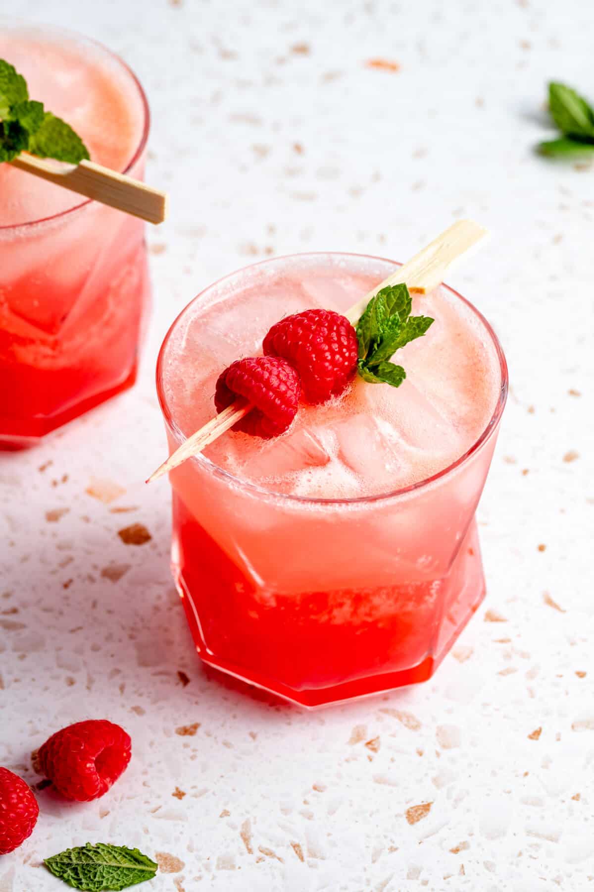 a tumbler glass filled with raspberry mocktail with raspberries on a skewer and mint leaves