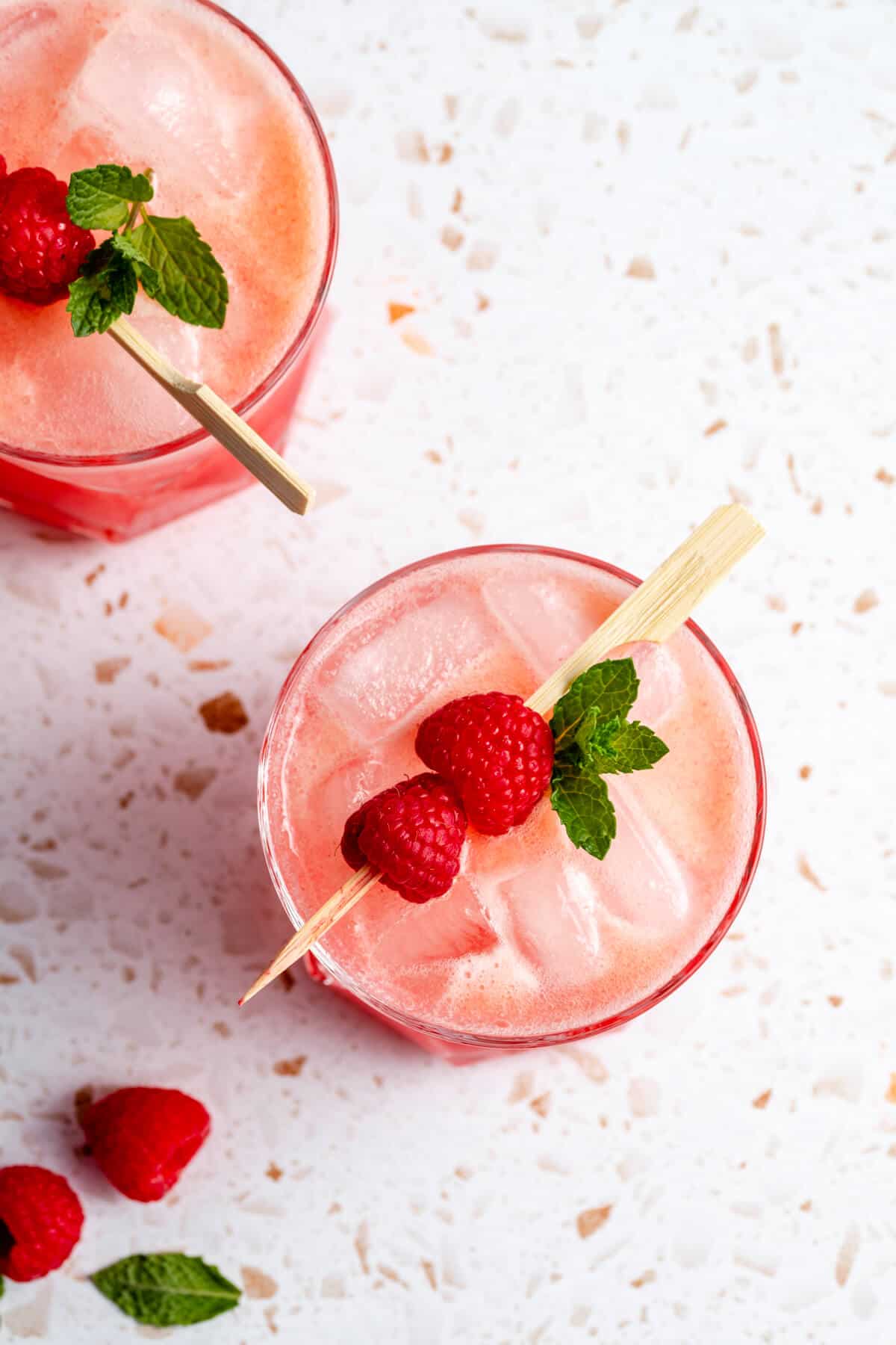 mocktail in a tumbler with ice floating on the top with raspberries on a skewer and mint leaves